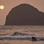 A dog splashes in the surf as the sun sets in front of Gull Rock off the coast of Cornwall. Pic: Ben Birchall/PA Images.