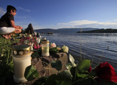 A woman sits among floral tributes to the victims of the shooting as she looks at Utoya island.
