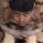 Pakistani Jaafar Sakhawat, 8, who works in a brick factory, looks up while taking a break, sitting on a pile of damaged bricks, on the outskirts of Islamabad, Pakistan, Wednesday, May 9, 2012. (AP Photo/Muhammed Muheisen)