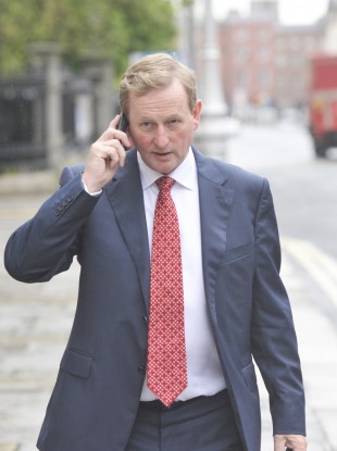 Taoiseach Enda Kenny doing a bit of mobile working of his own as he arrives at government buildings yesterday.